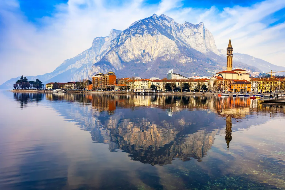 A beautiful image of a town and a mountain reflected on a calm lake in Lecco, a top pick when considering where to stay in Lake Como
