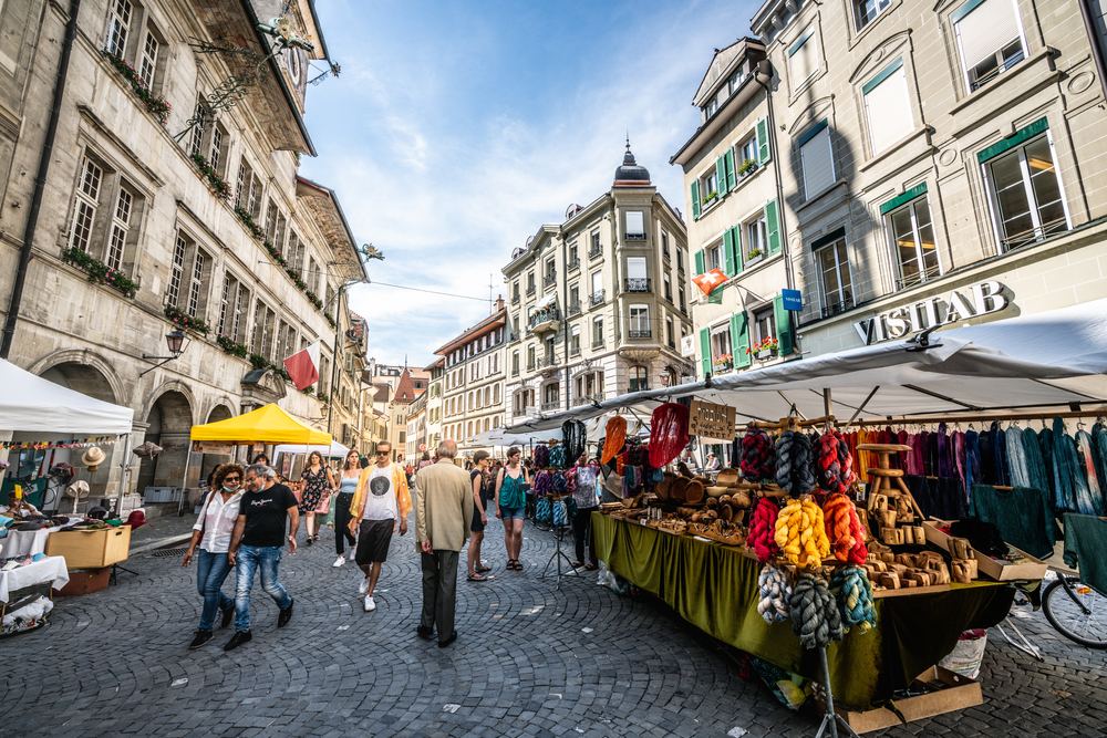 A street in Lausanne, Switzerland with store stall selling clothes and other items and people walking, snapped for a travel guide talking about the safety of visiting the country.