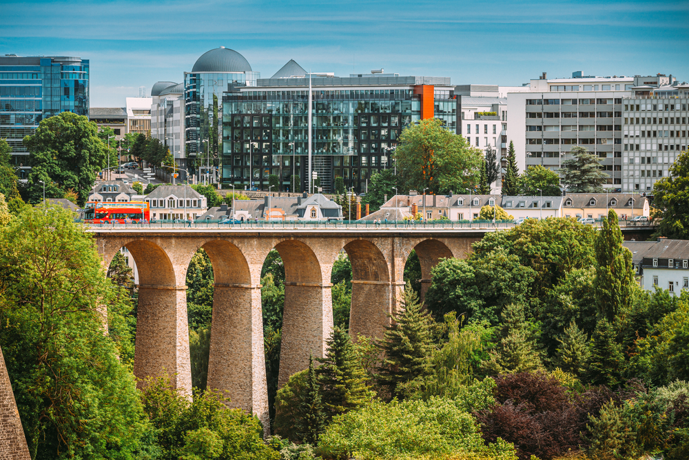 View of Ville Haute, Luxembourg City, one of the best areas to stay in Luxembourg, a  tall bridge with lush trees at the bottom and at a distance are modern city buildings.