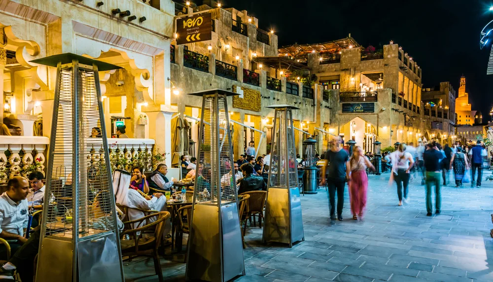 A restaurant on the side of the street at night where arabic people are seen eating. 