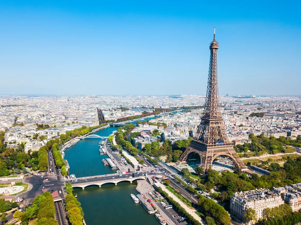 Aerial view of Paris and the Eiffel Tower in the Champs de Mars district by the Seine River on a clear sunny day for a list of the cheapest places to fly into for European travelers