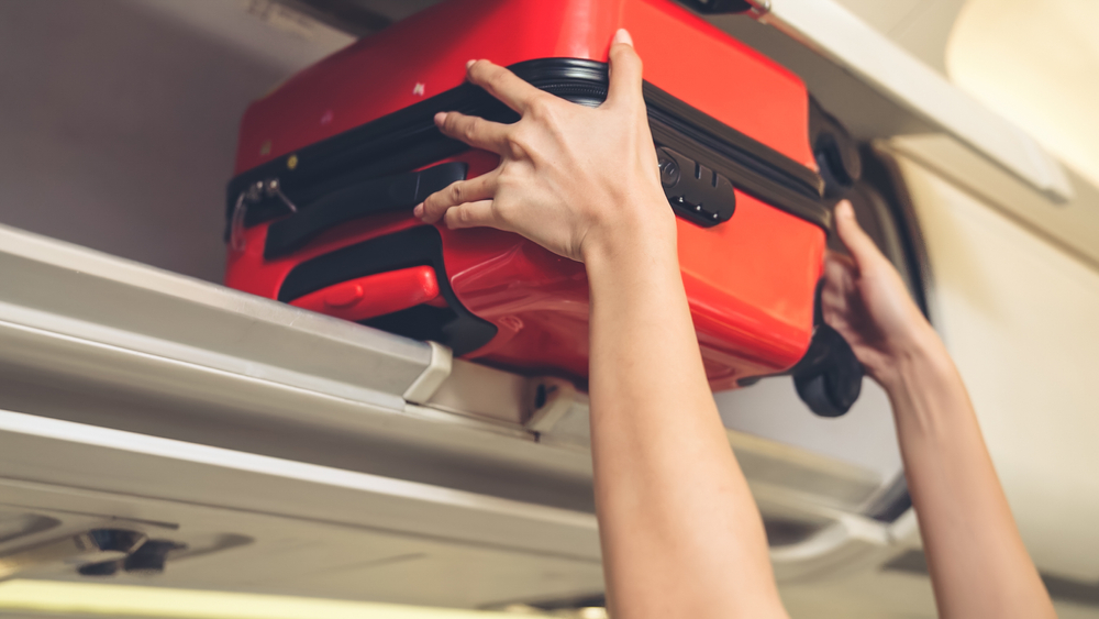 Airplane cabin crew places red luggage into the overhead bin before a flight, which passengers on Spirit Airlines will pay a fee for with 1 free personal bag included
