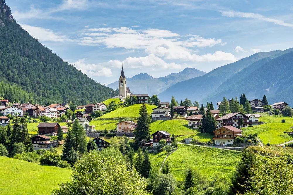 A peaceful town on a valley where houses can be seen be big lawns covered by green grass, an image for a travel guide about the safety in visiting Switzerland.