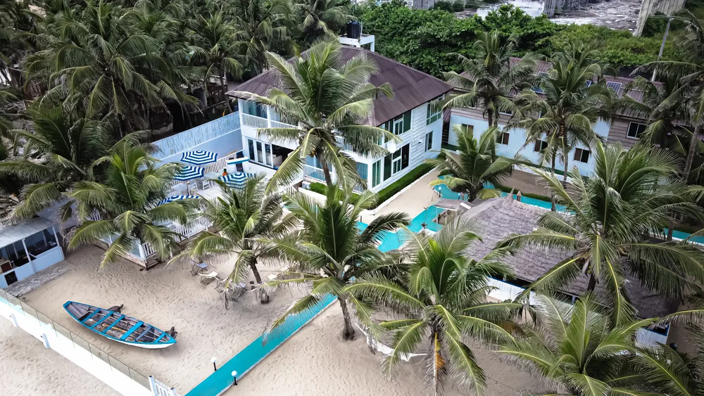 A small resort by the beach with coconut trees, an image for an article about trip cost to Nigeria, the property is fenced on the shore with 