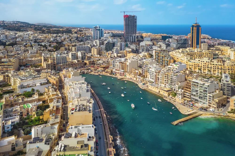 aerials of a populated city in St. Julian’s, one of the best areas to stay in Malta, structures varies from low to high rise and boats are on the gulf beside the city.