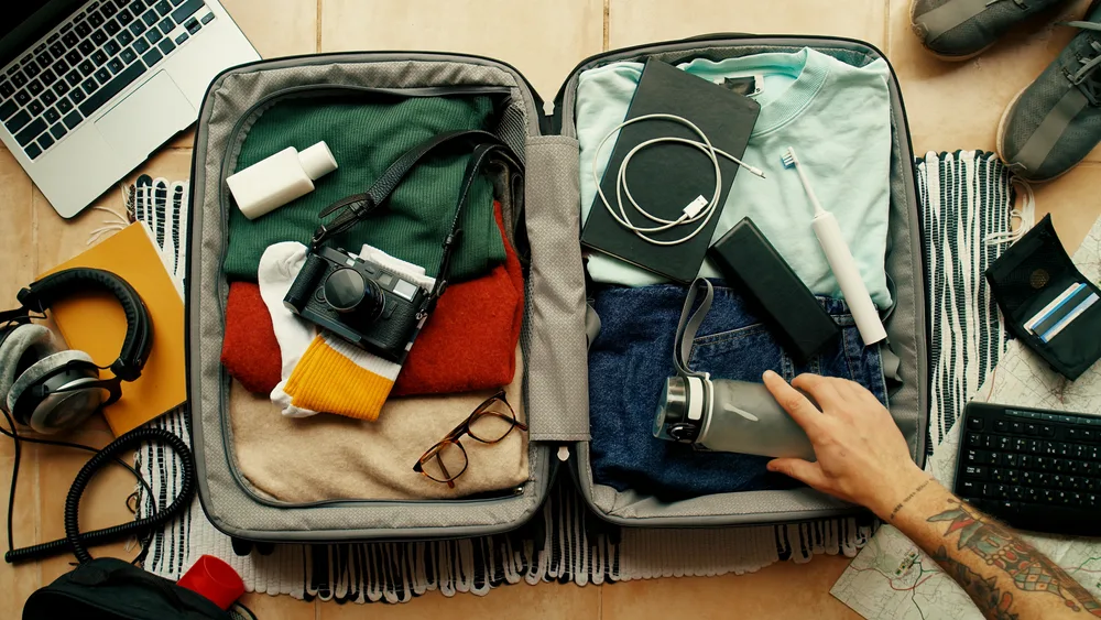 A man packing his suitcase with clothes and other essentials while preparing for a trip. 