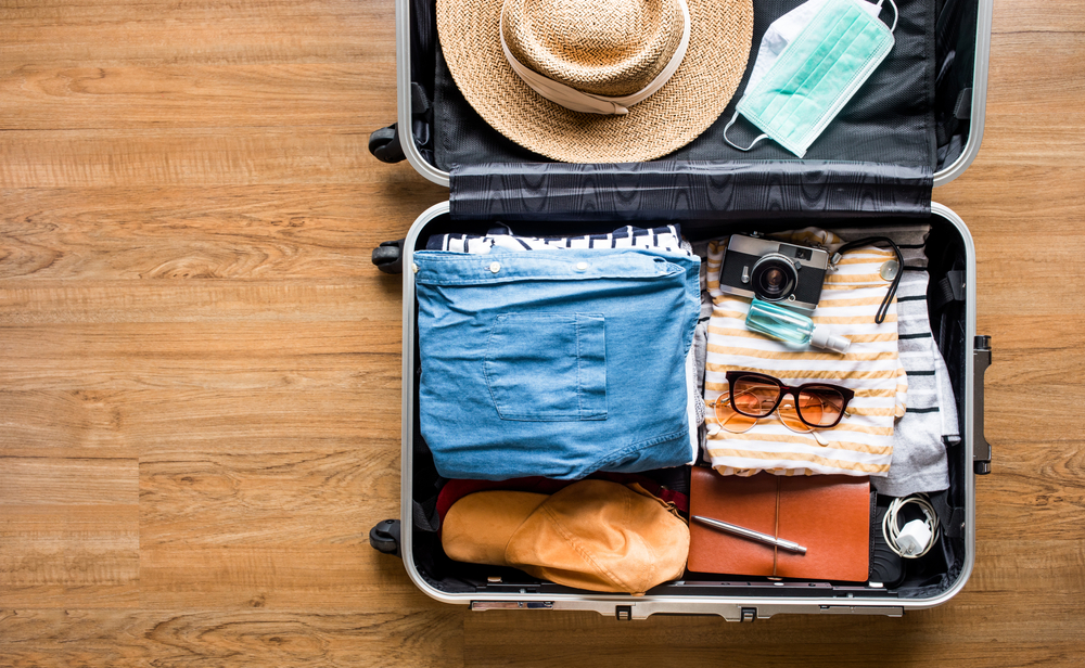 A packed luggage with clothes, hat, sunglasses, and camera.