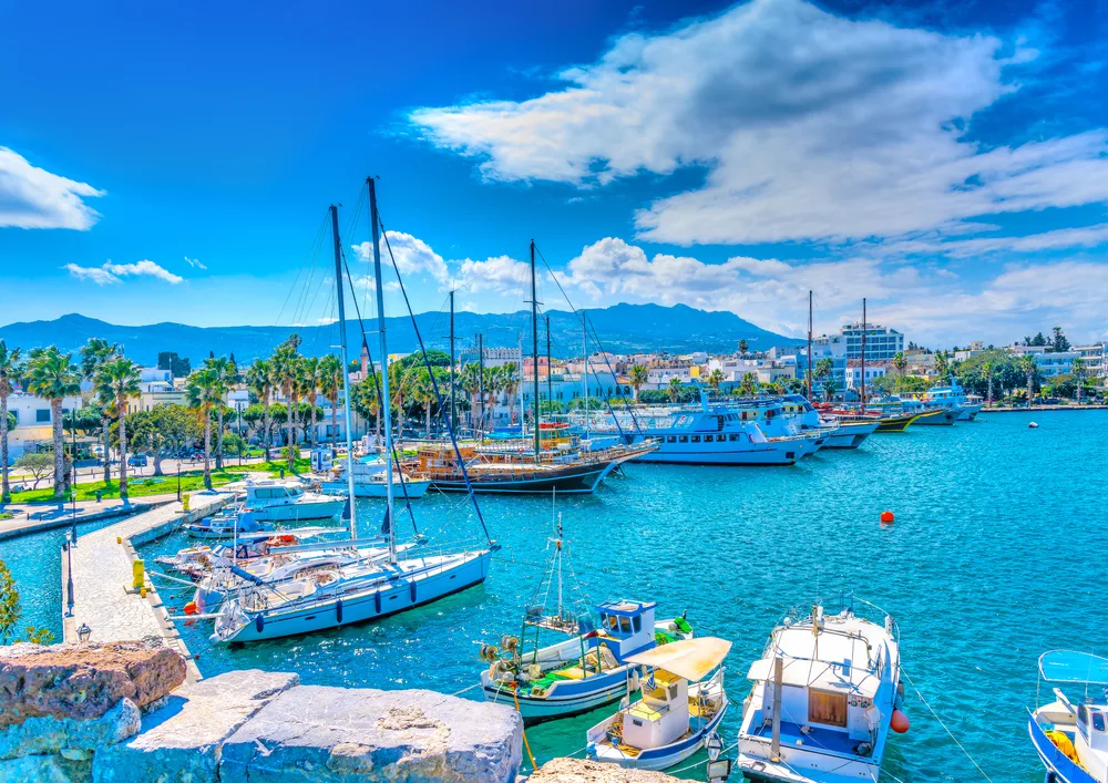 An adventurous vibe in a port in Kos, Greece, one of the best areas to stay in the Mediterranean, where sailboats are docked during a clear and calm afternoon.