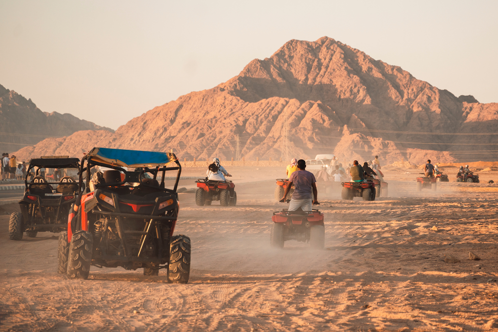 A group of friends riding their quad bikes in a desert and they are seen driving towards a desert mountain.