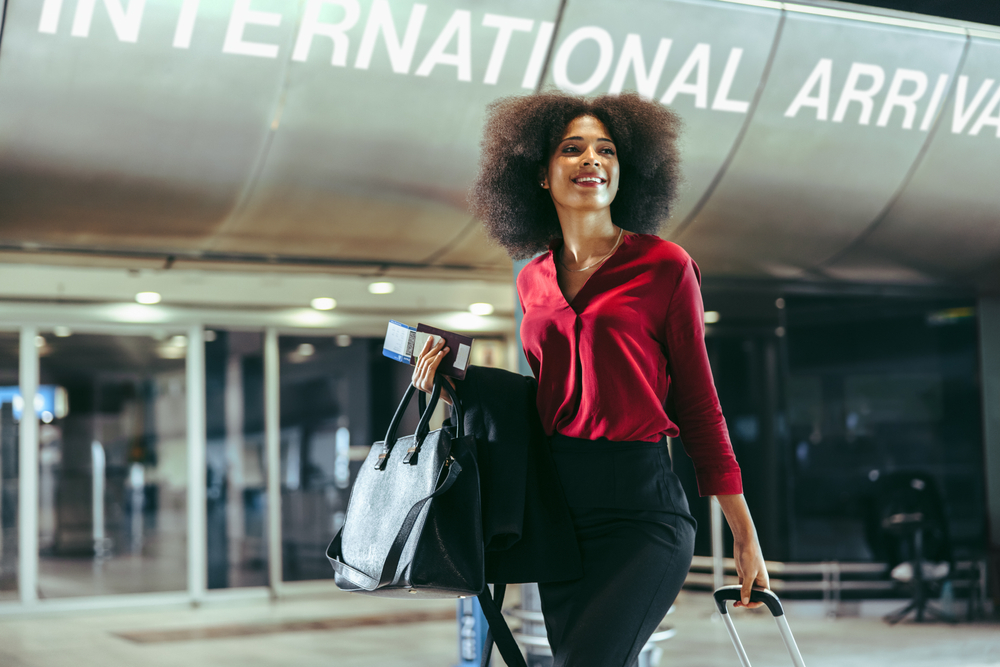 African American woman smiles as she enters the international arrival area at the airport with her luggage, packed according to the international travel checklist