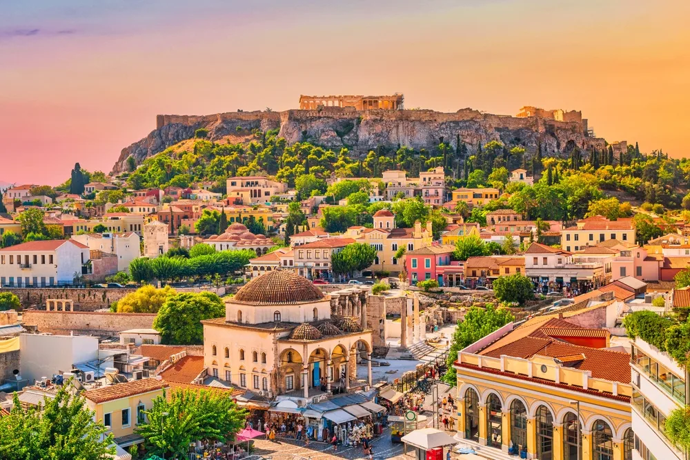 Aerial view of a city with a mixture of old and modern houses, and ruins can be seen on a plateau during sunset, an image for an item on the list of facts about Greece.