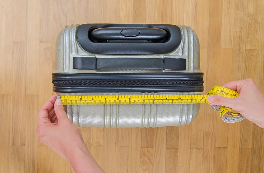 Concept of what luggage size incurs Spirit Airlines baggage fees with a close-up of someone measuring luggage with measuring tape before flying