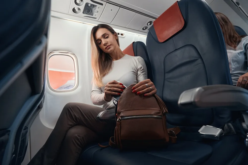 Woman sits in a plane seat with her free personal item as allowed by Frontier Airlines for a guide demonstrating the baggage fees for different types of luggage