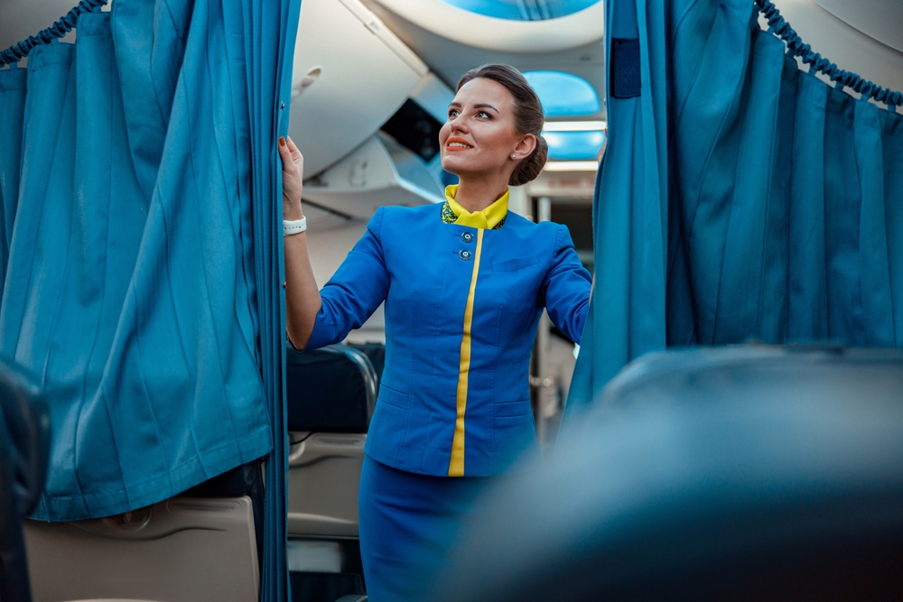 Smiling flight attendant closes curtain partition acting as the bulkhead on the plane for a guide showing what is a bulkhead seat for air passengers