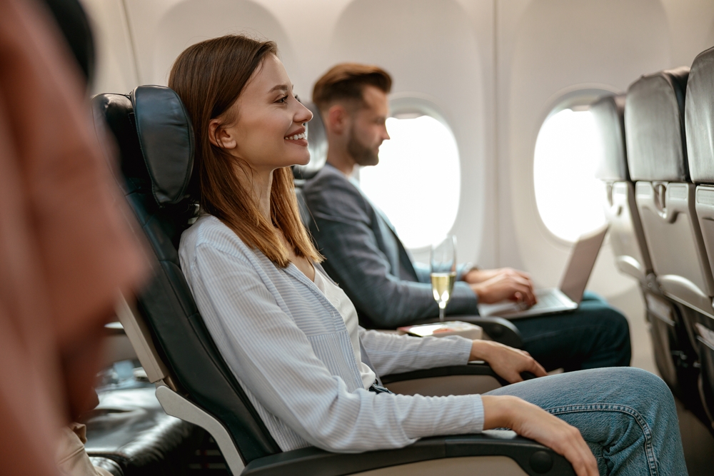 Woman smiles sitting in her aisle seat for a frequently asked questions section explaining how to get the best seat on a plane with plenty of room