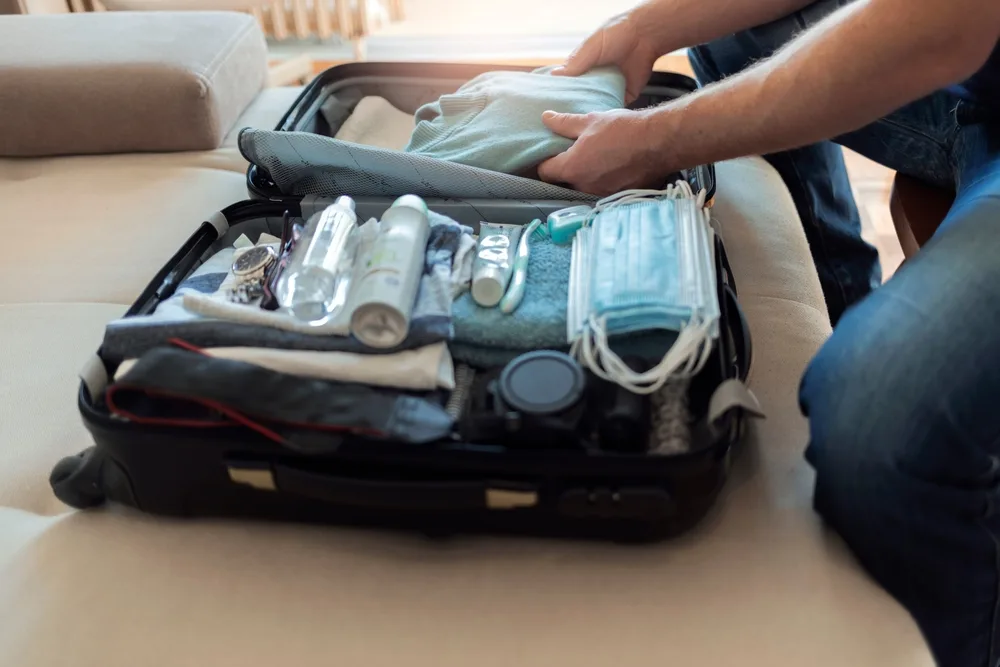 A man packing his suitcase with clothes, where at the top, personal care items, for a piece on a section of a guide about what to pack to Costa Rica.
