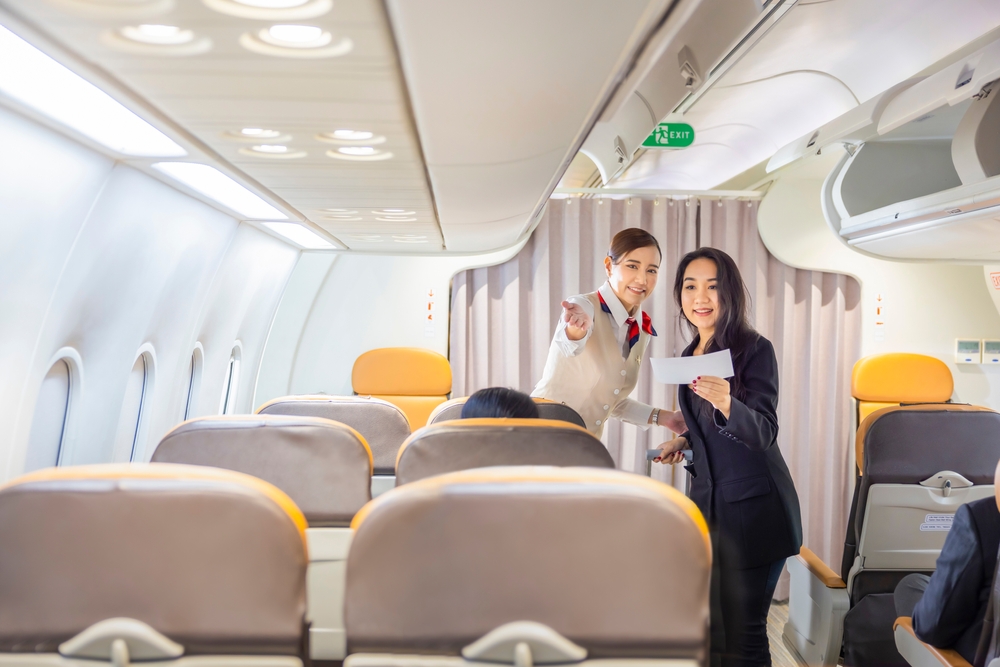 Asian flight attendant points to a seat on the plane for a business traveler to sit after assignment as she holds her boarding pass