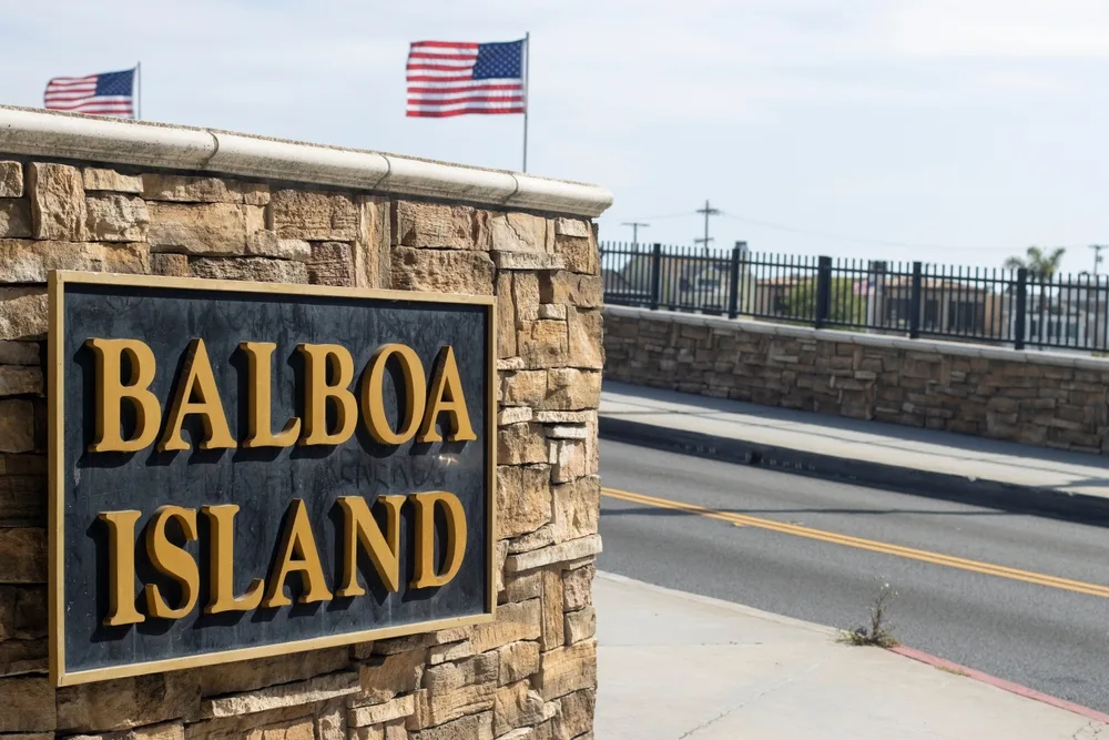A sign posted on a wall that says Balboa Island and two US flag can be seen in background. 