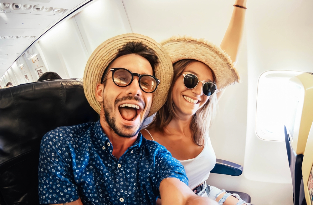 A couple taking a selfie while on board an airplane with happy faces. 