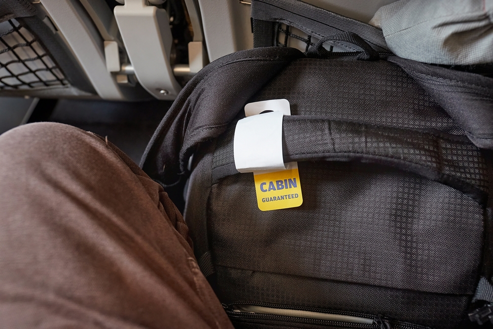 Man with a small carry on backpack tagged with a yellow Cabin Guarantee note shows how Spirit Airlines baggage fees can cover personal, carry on, and checked bags