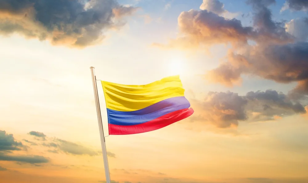 The flag of Colombia raised and waving on a pole during sunset. 