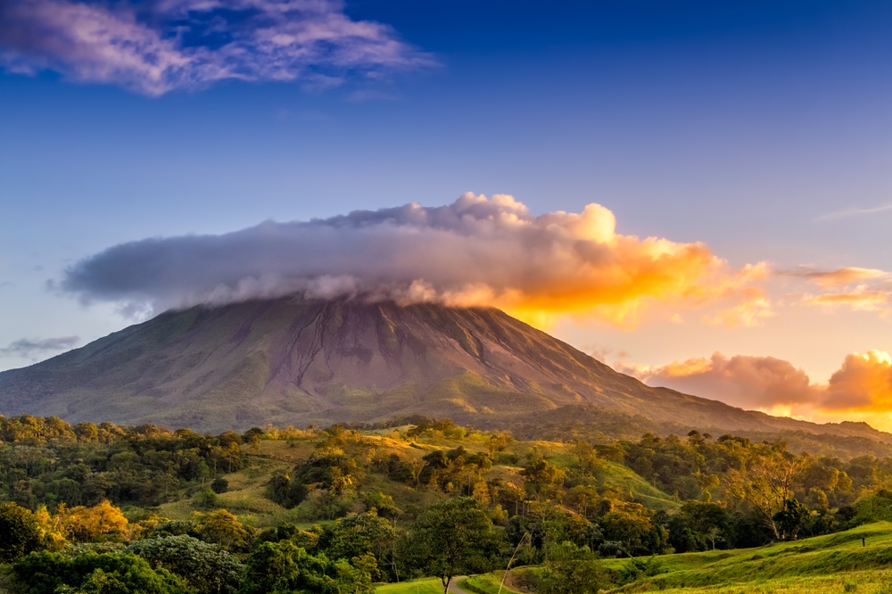 An extremely tall mountain where the peak can be seen covered with clouds during sunset. 