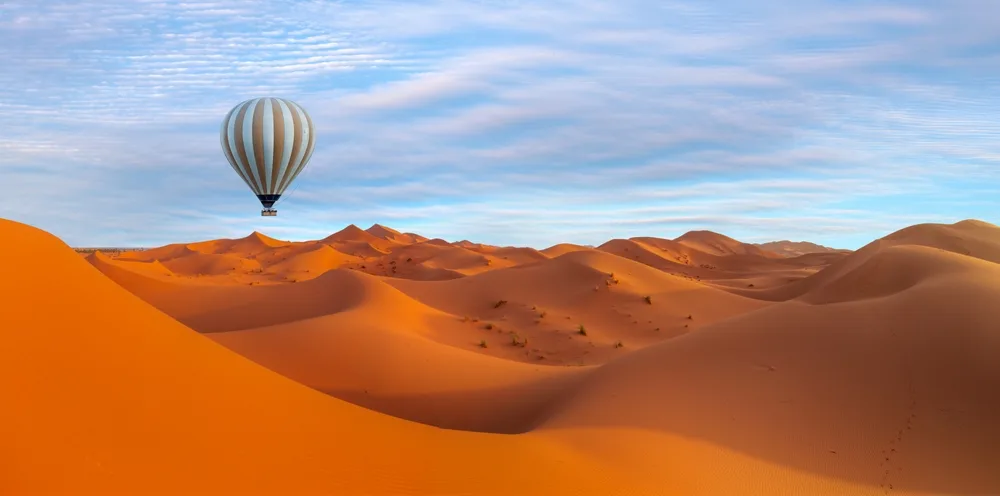 A hot air balloon hovering above a vast desert, an image for an article about trip cost to Morocco.