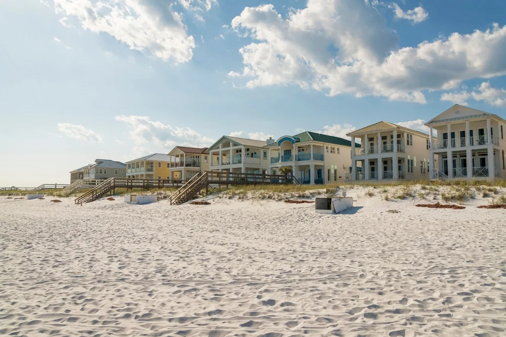 Two-story while beach houses fronting white sand beach can be seen during a hot summer afternoon. 