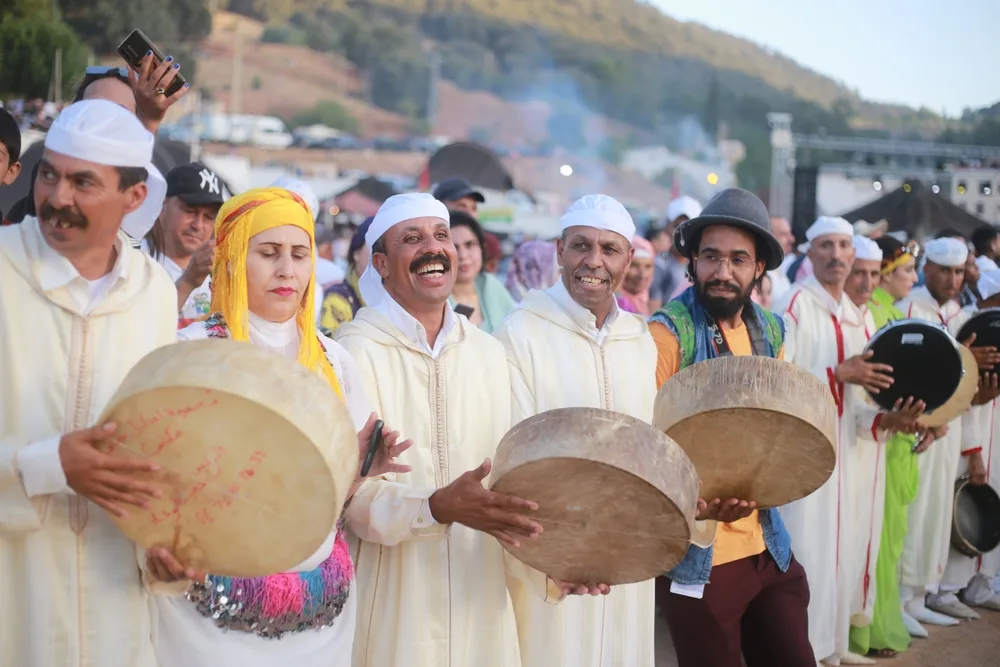 Locals holding a traditional musical instrument while wearing traditional clothes during a celebration, our pick for an article about trip cost to Morocco.