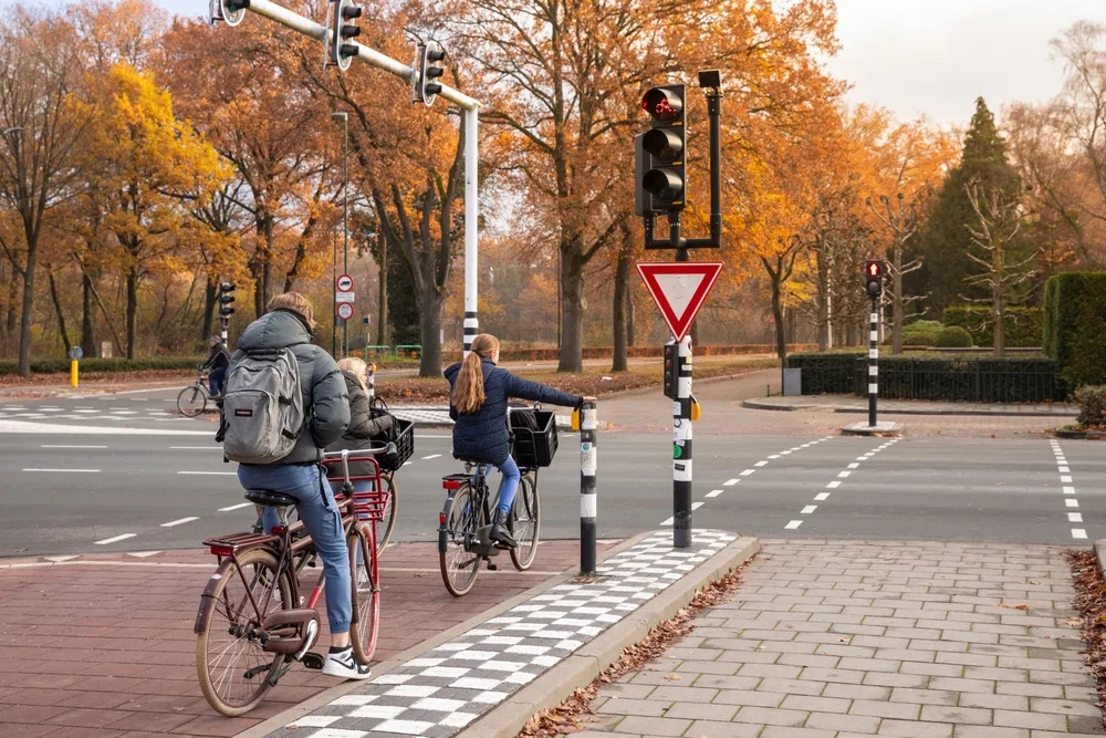 Three people can be seen using the bike lane, while the first one ahead is signalling to go right using her hand, an image for the guide safety in visiting the Netherlands.