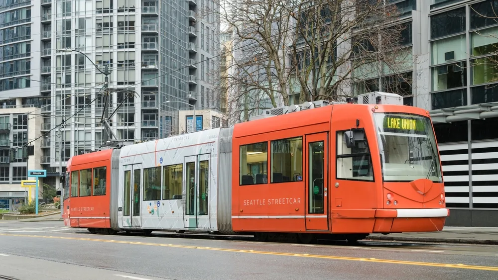 An orange cabe car running on its tracks within a city. 