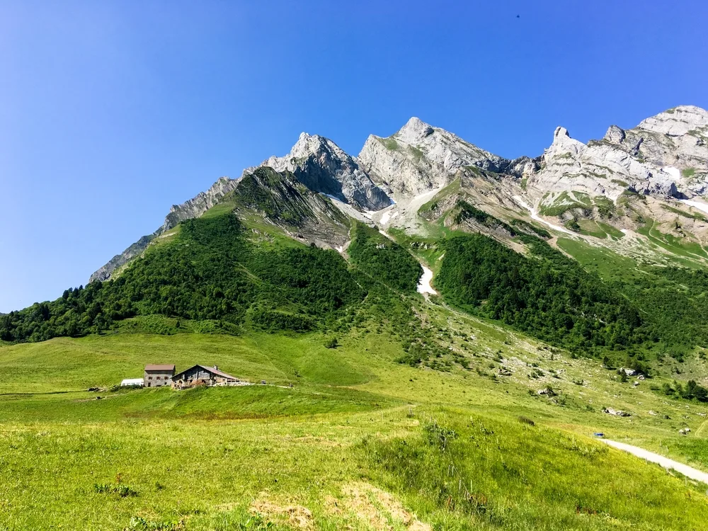 A lonely house can be seen near the foot of a tall mountain with ice caps in The French Alps, one of the best areas to stay in France.