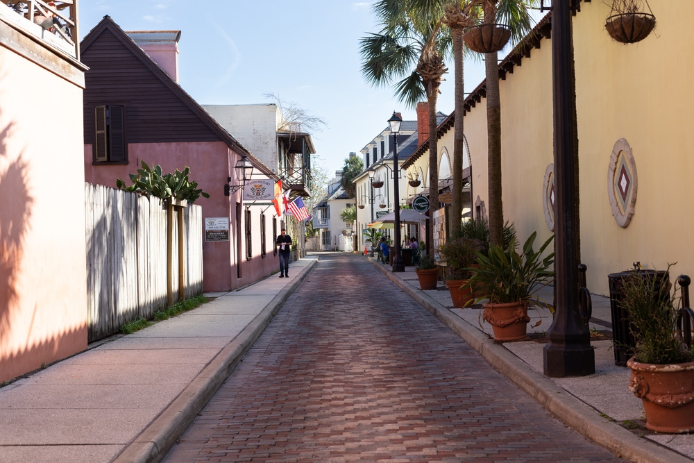 A narrow street with brick pavement and palm trees on the side. 
