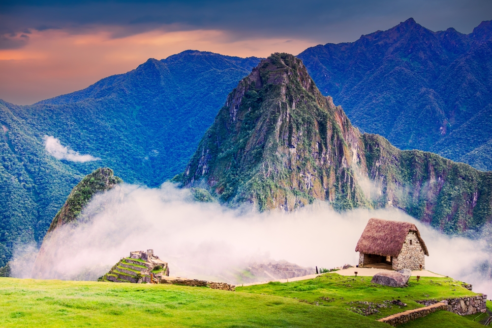 Fog hovering at the peak of the mountain, where a small stone cabin can be seen with green fields, an image for an item on the list of facts about Peru.