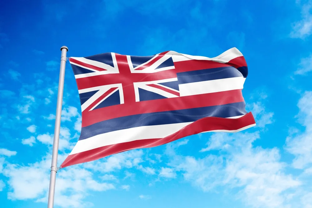 A Hawaii flag waving in the air with the blue sky in background.