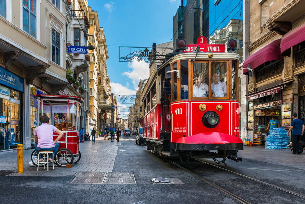 Image for a piece describing the average trip to Turkey costs, the Taksim-Tunel Nostalgia Tram makes its way down a historic part of town with peddlers standing in and outside of their market stores