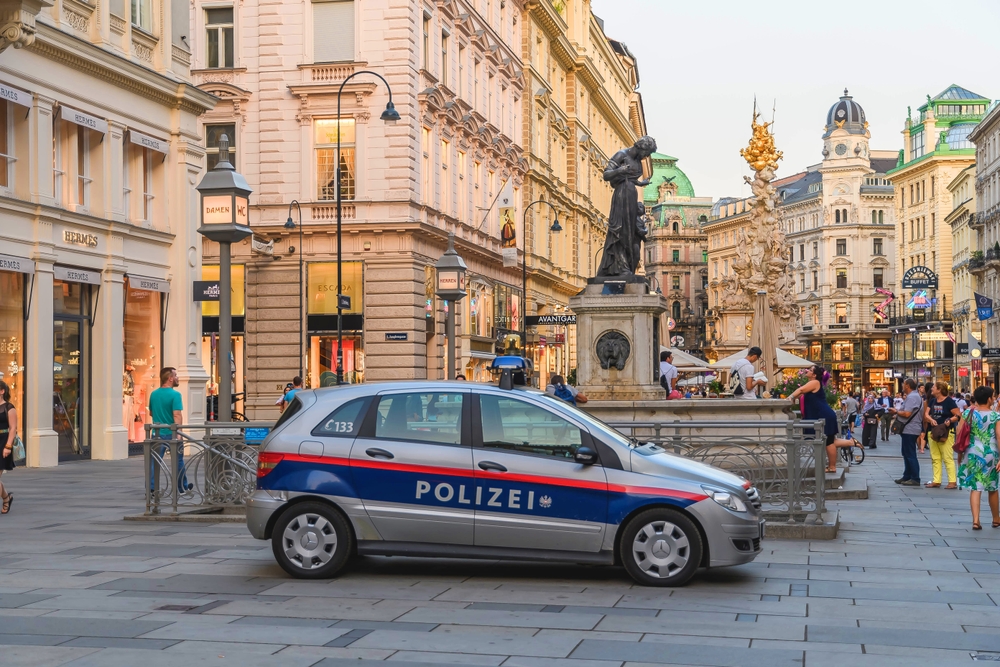 A police car parked on the street surrounded by old structures  and several people walking, a section image about avoiding bad area in an article about safety in Vienna.