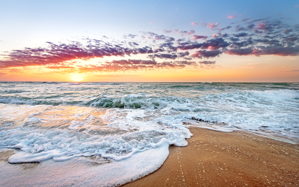 East coast Florida beach with golden brown sand as waves wash ashore at sunrise for a section detailing how long a flight to Florida takes from the Midwest