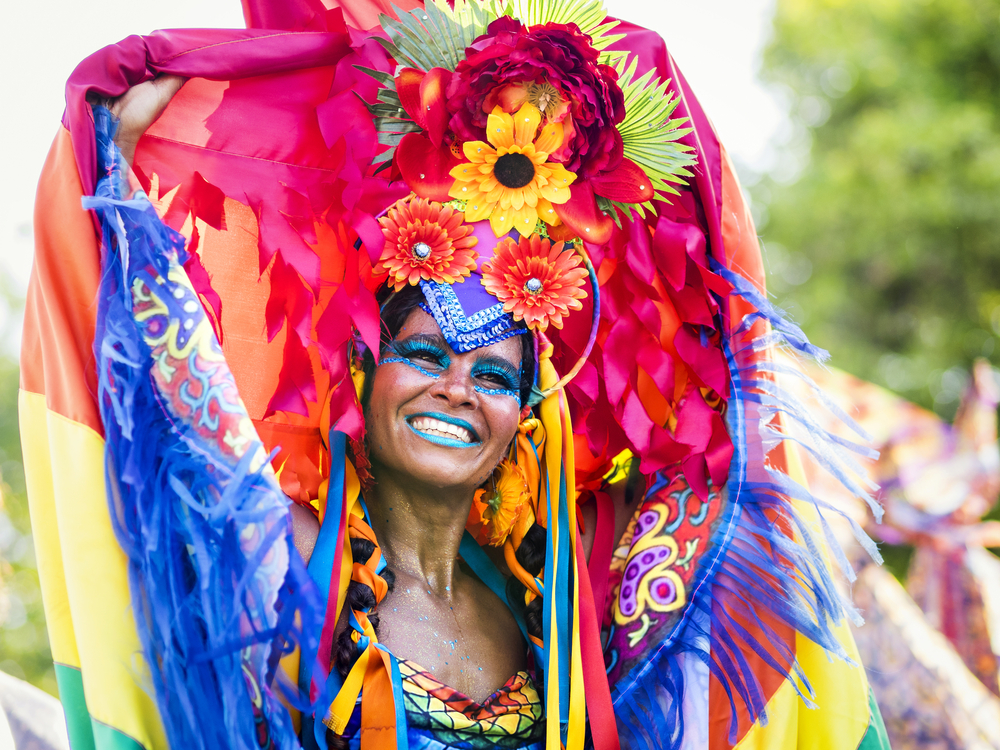 A woman dancing on a festival where she is wearing vibrant clothes and a floral headdress.