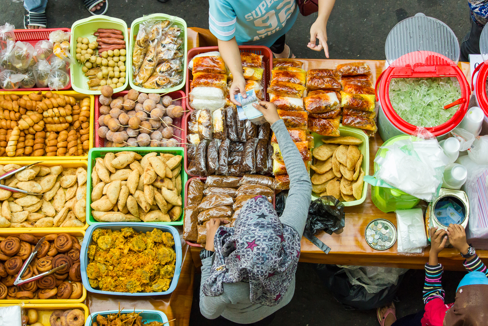 A costumer paying for an older in a street food stall, where various foods are placed in trays. 