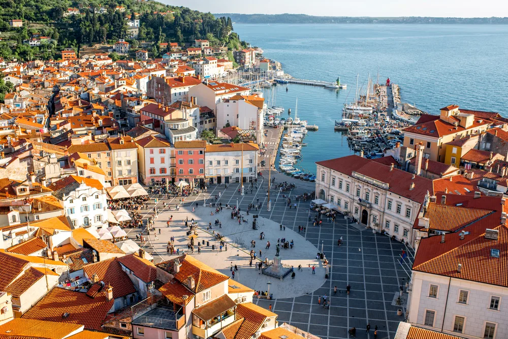 A town square near the pier where people gathered, structure with orange roofing surround the square, an image for a travel guide about safety in visiting Slovenia.