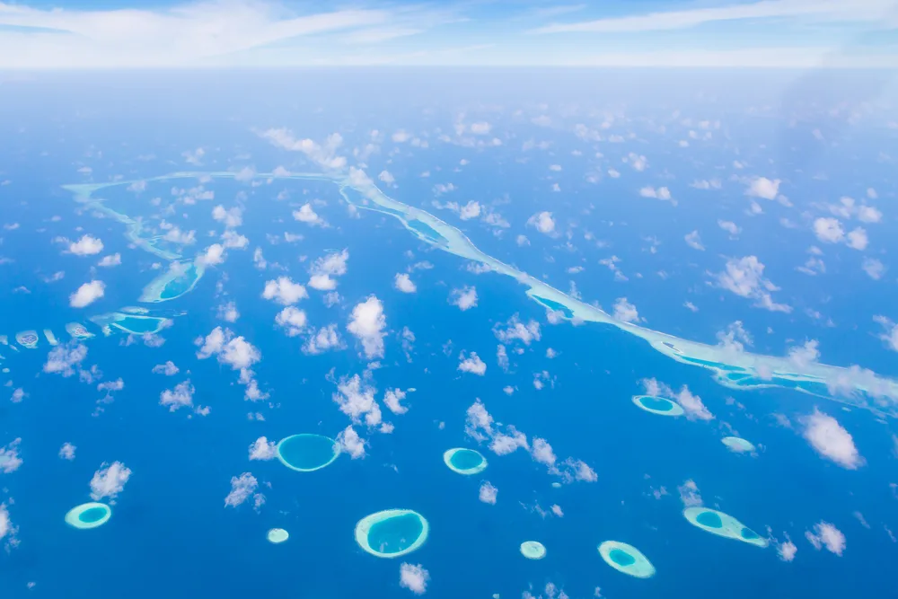 Aerial view of a group of atolls in the Maldives as seen from a plane on a beautiful, clear day for a guide answering how long is a flight to the Maldives?