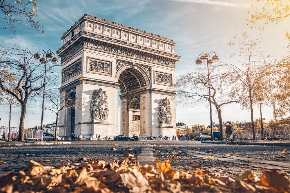 View of the Arc de Triomphe with fallen leaves on the ground and clear skies to show the #2 cheapest place to fly into Europe