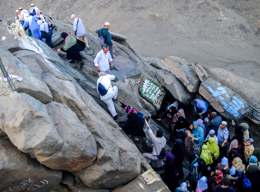 Muslim people climbing on rocks for passage during a pilgrimage, a section image for an article about trip cost to Mecca.