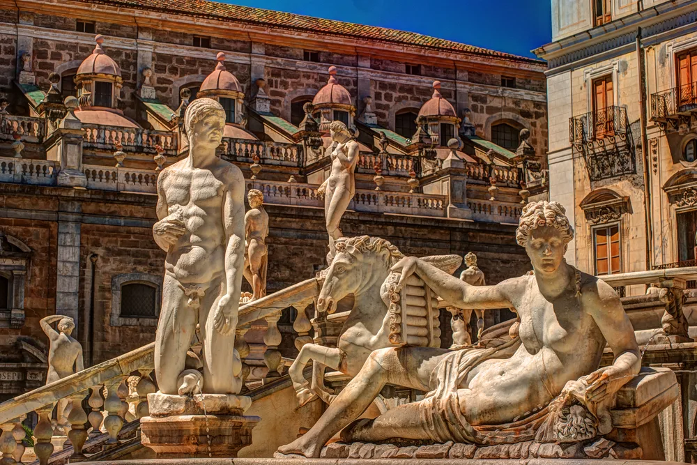 Classic sculpture of naked men and women beside an old building, captured for a piece on a travel guide about trip cost to Sicily.