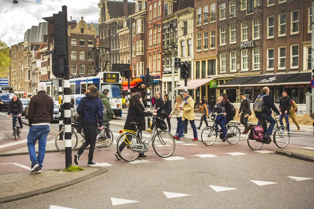 People crossing a street during a red light where some are seen walking and others are on their bicycles, an image for a section about crime in the Netherlands in a guide about the safety in visiting the country.