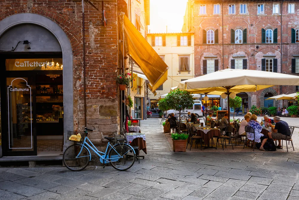 A peaceful morning in a cafe where old people are enjoying the meal outside, and a bicycle is parked at the front, a section image for a travel guide about safety in visiting Tuscany.