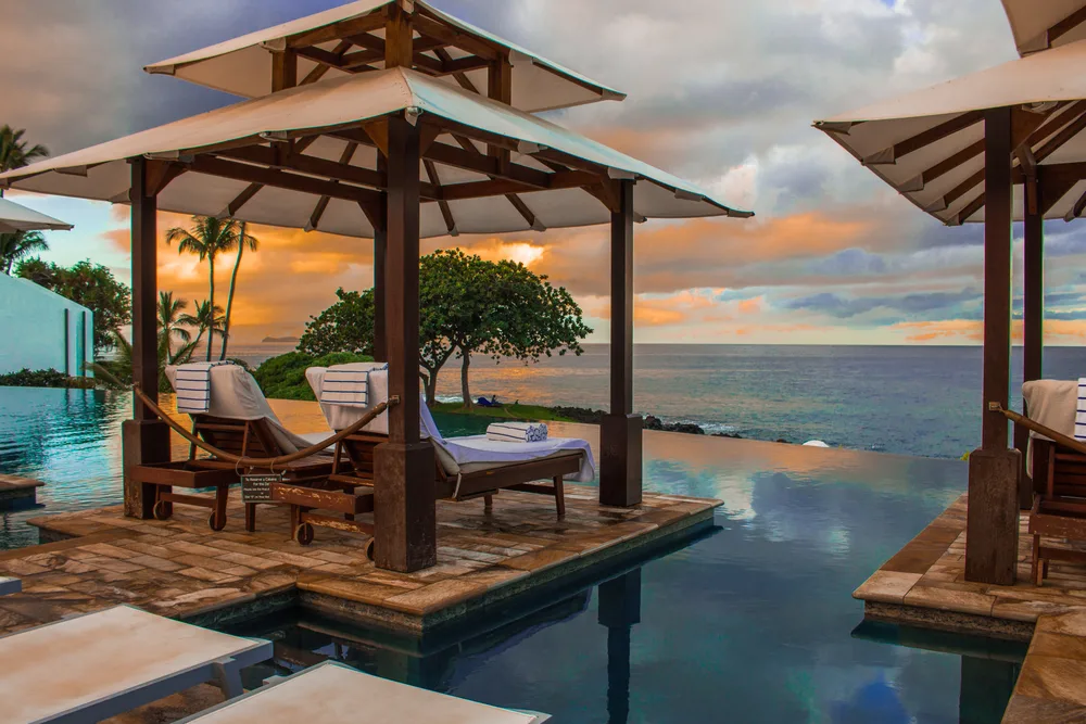 A cabana by the pool with a relaxed view of the sea during sunset.