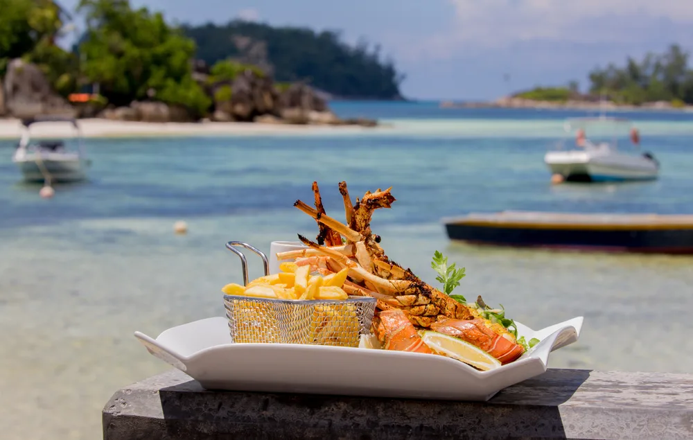 A meal prepared on a plate with lobster and fries placed on a concrete near the beach.