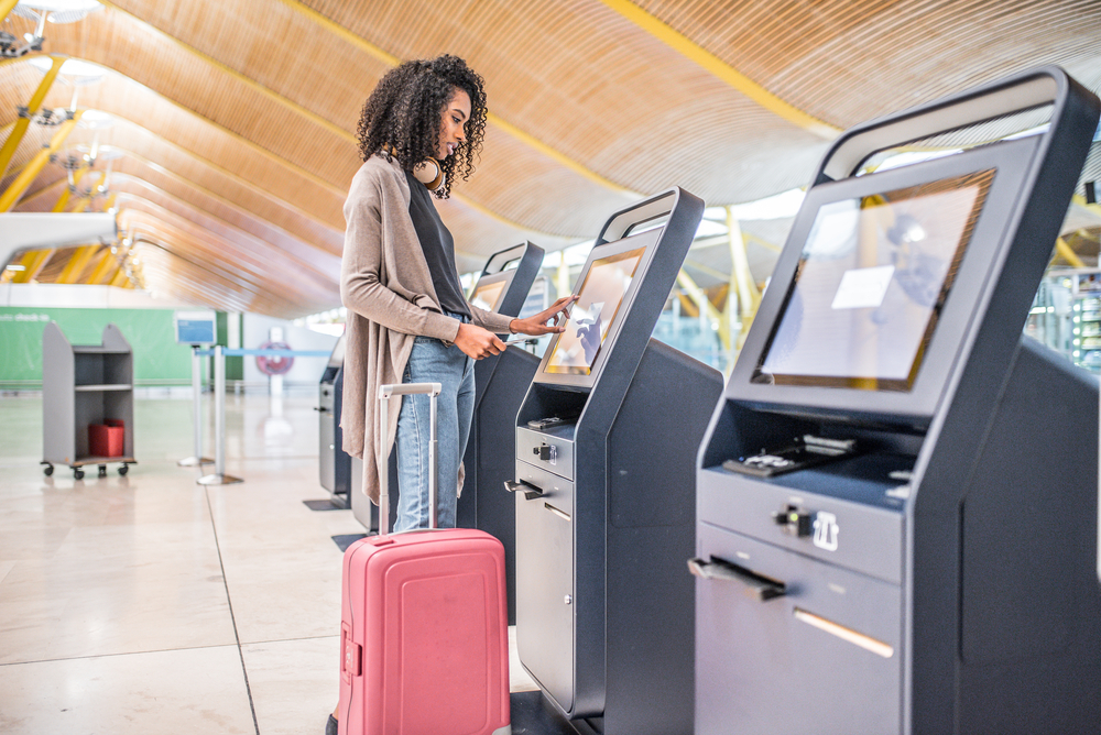 Young African American woman uses an airport kiosk with her luggage at her side for a piece answering what is a standby flight?